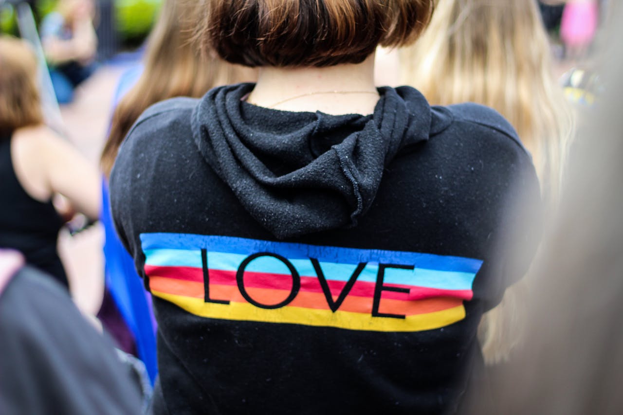 Person wearing a vibrant LGBT pride-themed hoodie with 'love' print at a festival.